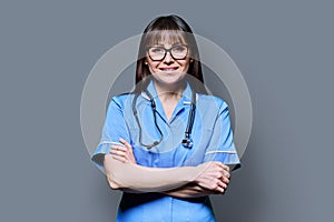 Portrait of smiling woman nurse in blue with stethoscope on grey background