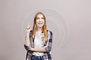 Portrait of a smiling woman pointing finger up at copy space isolated over gray background