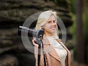 Portrait of a smiling woman professional photographer in a summer park. A woman with a camera in his hands looking at the camera