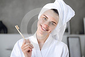 Portrait of smiling woman in robe holding bamboo toothbrush