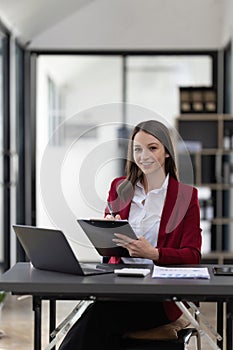 Portrait smiling woman sitting at desk working on laptop taking notes in notebook, happy millennial female working