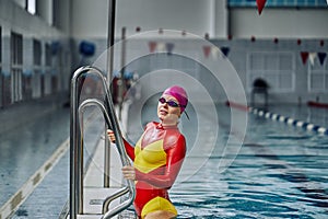 Portrait of a smiling woman swimmer in red yellow swimsuit in the pool