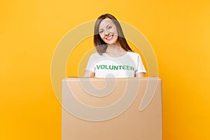 Portrait of smiling woman in white t-shirt with written inscription green title volunteer with big cardboard box