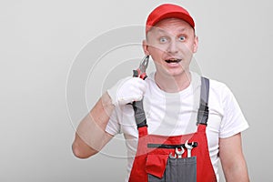 Portrait of a smiling worker in red uniform, cap and white glove is having fun with pliers, isolated on white background. Work