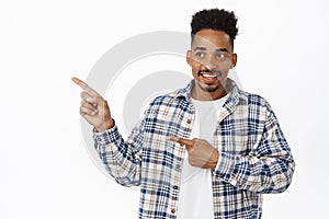 Portrait of smiling young african american man, pointing fingers left and looking at logo with happy face, reading promo