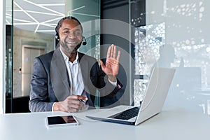 Portrait of a smiling young African American man in a suit sitting at a desk in a headset and in front of a laptop