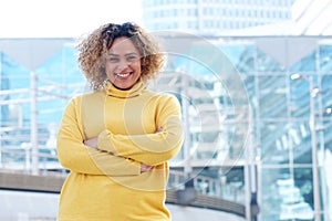 Smiling young african american woman with curly hair and arms crossed in city