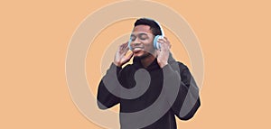 Portrait of smiling young african runner man in wireless headphones enjoying listening to music wearing black hoodie isolated on