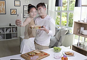 Portrait of a smiling young Asian couple taking a selfie while cooking together at the kitchen