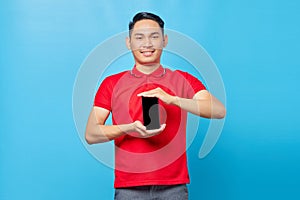 Portrait of smiling young asian man showing blank screen mobile phone isolated on bluebackground