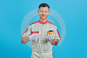 Portrait of smiling young Asian mechanic carrying cup of coffee in hand over blue background