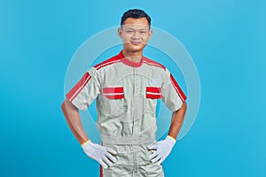 Portrait of smiling young Asian mechanic holding hands confidently over blue background