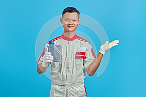 Portrait of smiling young Asian mechanic showing machine oil plastic bottle and pointing to copy space with palm over blue