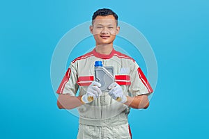 Portrait of smiling young Asian mechanic showing plastic bottle of engine oil in hand isolated on blue background