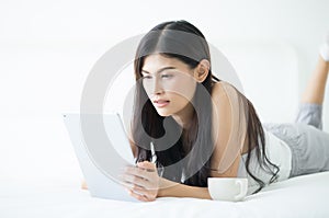 Portrait of a smiling young Asian woman using tablet in the bed