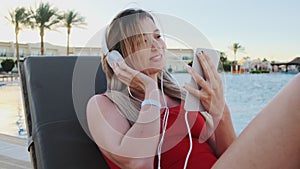 Portrait of smiling young attractive young woman in red bikini listening music from her smartphone in white headphones