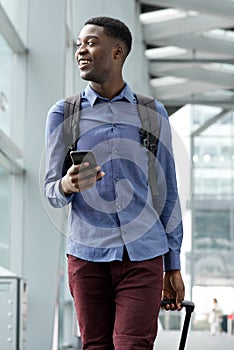 Smiling young black man traveling with bags and mobile phone