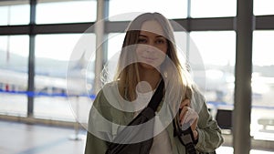 Portrait of smiling young blonde girl traveller walks with backpack by airport terminal