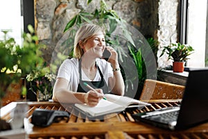 Portrait of smiling young botanist holding a fresh flower plant in pot in gardening center. Successful botanist and