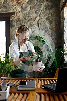 Portrait of smiling young botanist holding a fresh flower plant in pot in gardening center. Successful botanist and