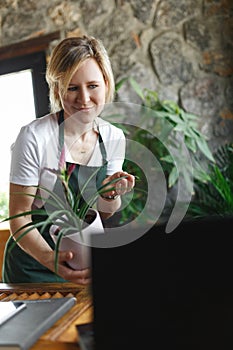 Portrait of smiling young botanist holding a fresh flower plant in pot in gardening center. Successful botanist and