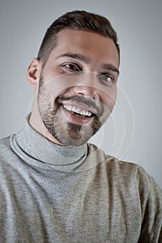 Portrait of a smiling young brown-haired man with a short beard and a gray turtleneck sweater