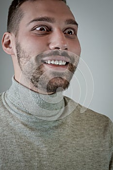 Portrait of a smiling young brown-haired man with a short beard and a gray turtleneck sweater