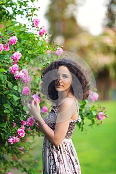 Portrait of a smiling young brunette Caucasian beautiful woman near rose bush, vertical, waist up