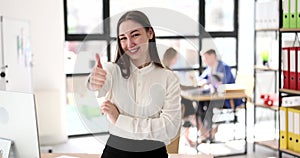 Portrait of smiling young business woman showing thumbs up and giving recommendation