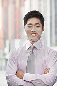 Portrait of smiling young businessman with arms crossed outdoors, Beijing, China