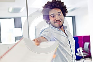 Portrait of smiling young businessman giving document in office