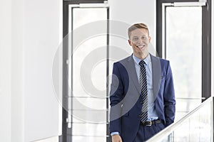 Portrait of smiling young businessman standing against window at office