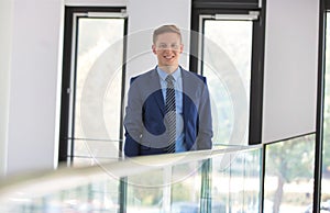 Portrait of smiling young businessman standing against window at office
