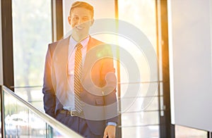 Portrait of smiling young businessman standing against window at office