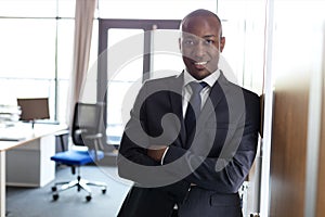 Portrait of smiling young businessman standing arms crossed leaning on cupboard in office