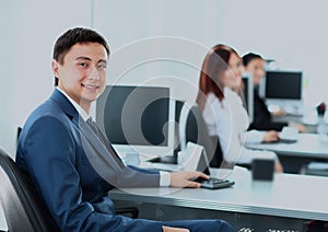 Portrait of a smiling young businessman working on computer at office with his colleagues.