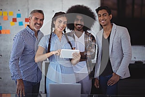 Portrait of smiling young businesswoman explaining over digital tablet to colleagues