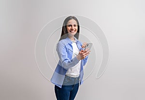 Portrait of smiling young businesswoman holding mobile phone and glasses against white background