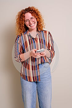 Portrait of smiling young businesswoman with redhead texting over smart phone on white background