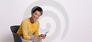 Portrait of smiling young businesswoman using smart phone and sitting on chair over white background