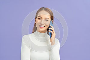 Portrait of a smiling young casual brunette woman talking on mobile phone isolated over violet background