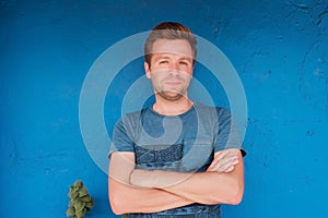 Portrait of smiling young caucasian man standing near blue wall with freen leaf