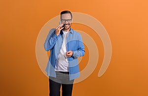 Portrait of smiling young confident businessman discussing over phone call on orange background