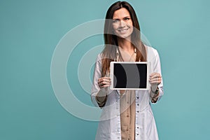 Portrait of smiling young doctor in white coat showing the screen of digital tablet in her hand.