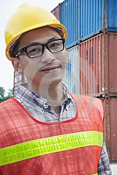 Portrait of smiling young engineer in protective workwear outdoors in a shipping yard