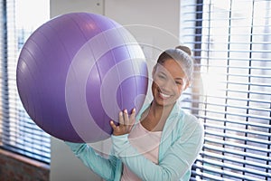 Portrait of smiling young female doctor holding purple exercise ball