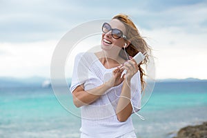 Portrait of a smiling young girl with earphones listening to music outdoors by the beach with ocean blue sky background