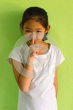 Portrait of a smiling young girl with her finger over her mouth.