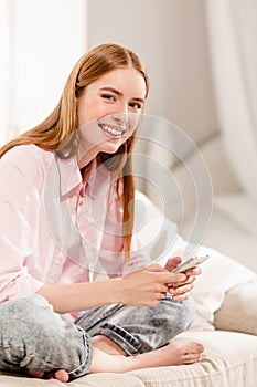 Portrait of smiling young girl in pink shirt, sitting on couch.