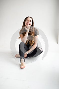 Portrait of a smiling young girl sitting with legs crossed on white background